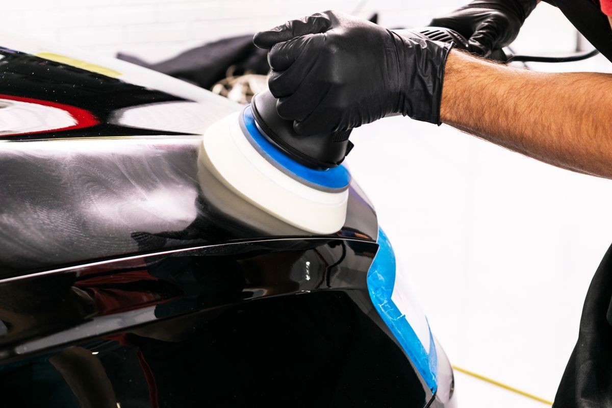 Car polish wax worker hands applying protective tape before polishing. Buffing and polishing car. Car detailing. Man holds a polisher in the hand and polishes the car